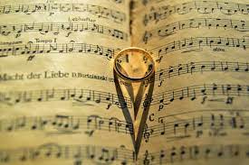 Old sheet music with a gold ring on the center creating a heart with its shadow.